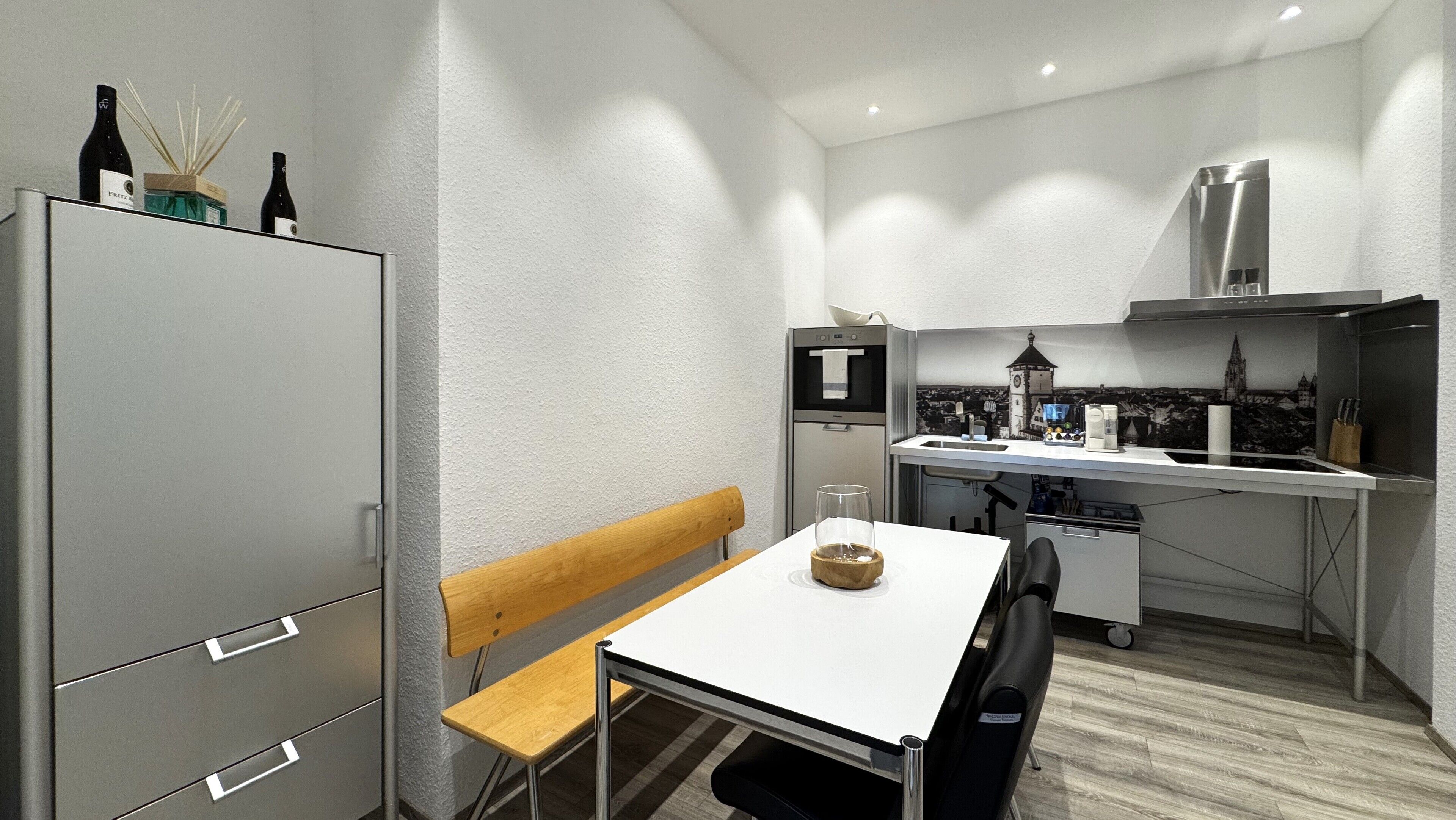 Une cuisine compacte avec un coin repas comprenant un banc, une table et un réfrigérateur.