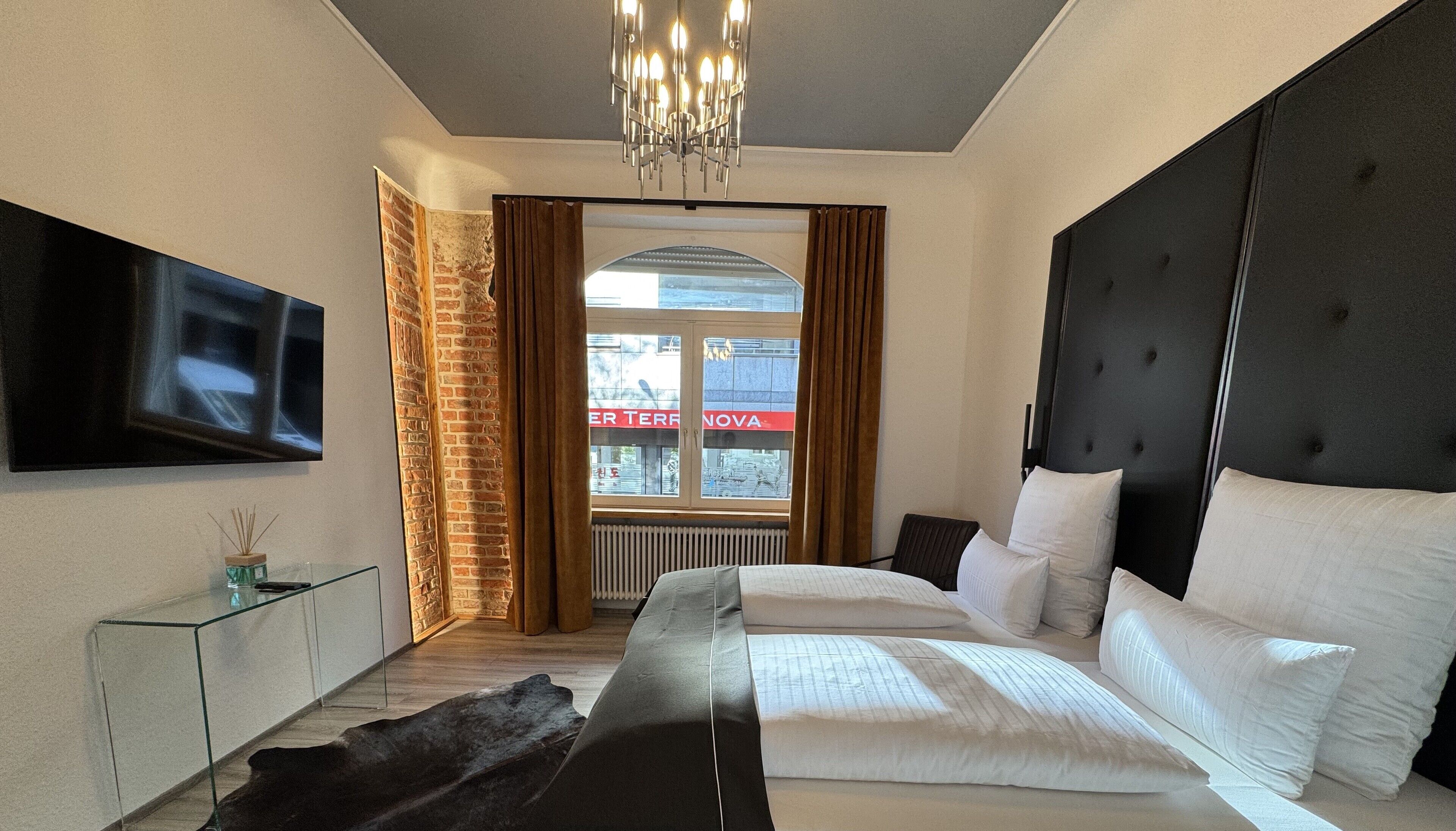 A modern bedroom with a large bed, a TV mounted on the wall, and a view of a building outside.