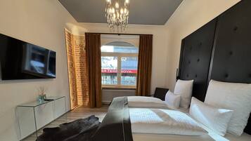 A modern bedroom with a large bed, a TV mounted on the wall, and a view of a building outside.