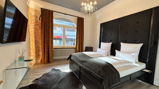 Ett modernt hotellrum med en stor säng, en tv som är monterad på väggen och utsikt över staden genom fönstret.