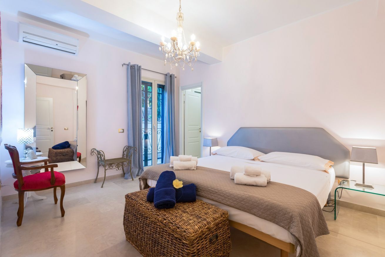 A bedroom with a large bed, a chair, a small table, a mirror, and a chandelier.
