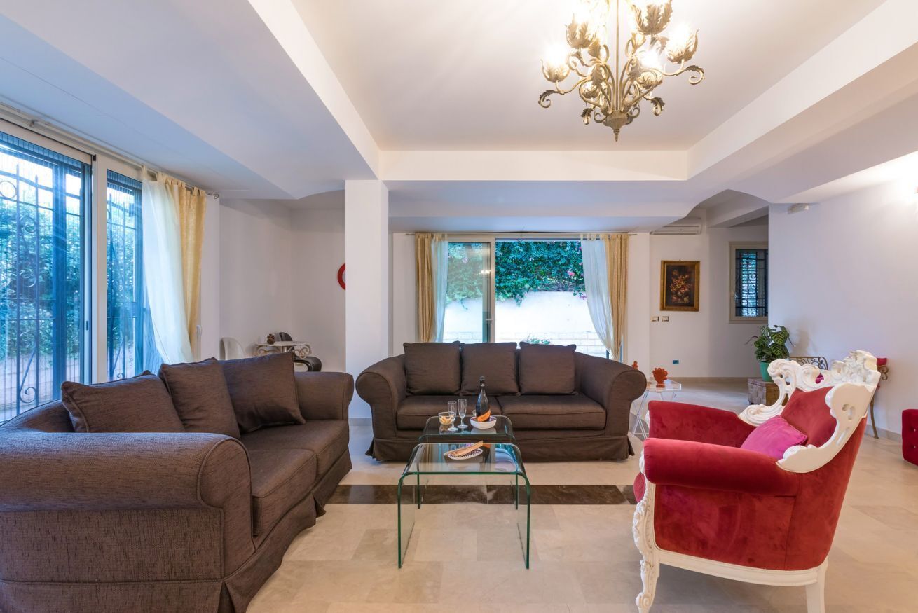 A living room with two sofas, a glass coffee table, a red armchair, and a chandelier.
