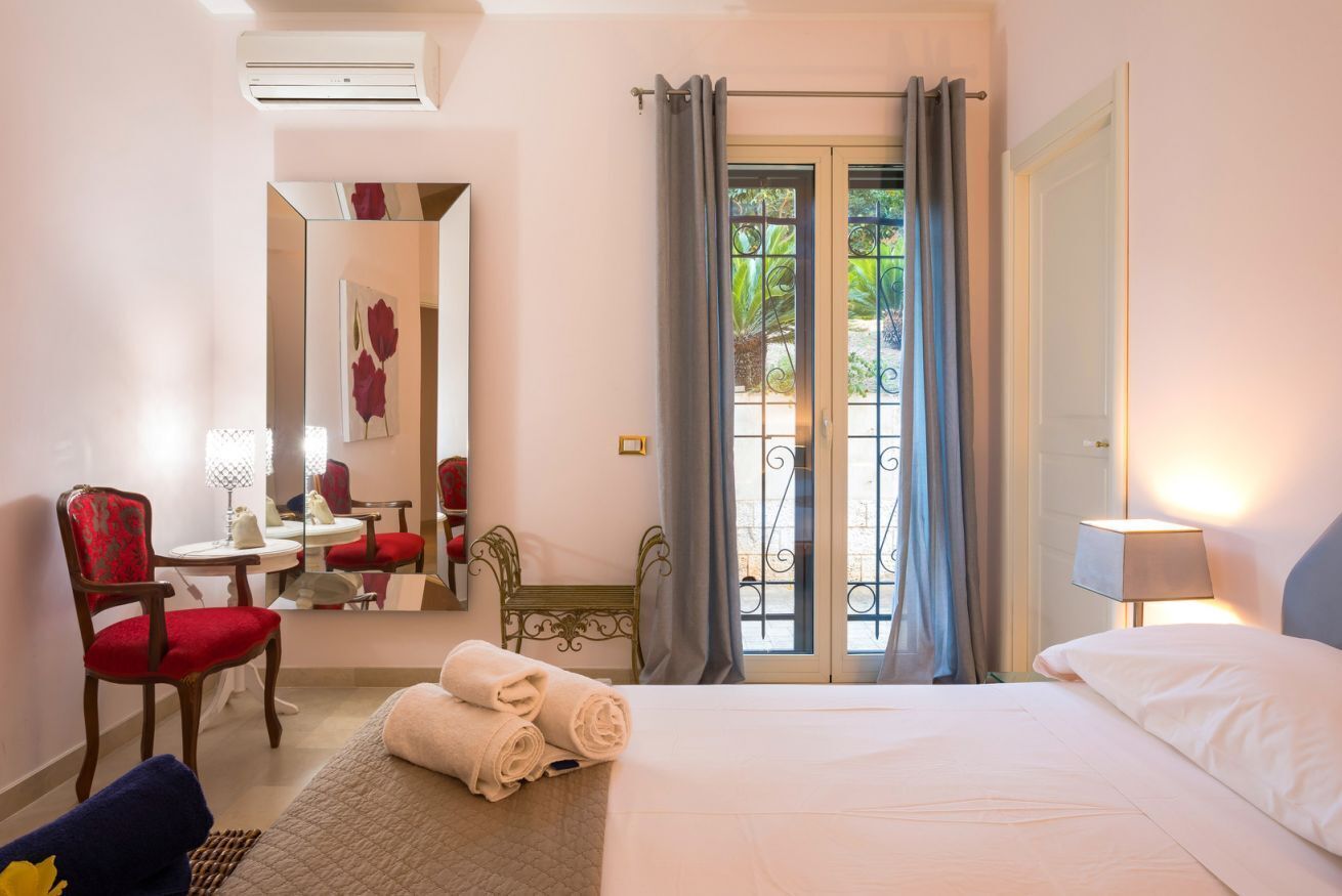 A hotel room with a bed, a chair, a desk, a mirror, and a window with curtains.