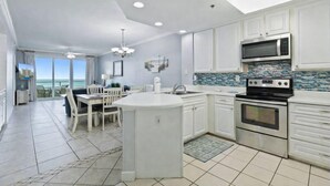 A modern kitchen with white cabinetry, a central island, stainless steel appliances, and a view to the outside. - Stunning 3BR Beachfront Condo - Heated Pool - Orange Beach Enclave #405 (Orange Beach)