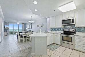 A modern kitchen with white cabinetry, a central island, stainless steel appliances, and a view to the outside. - Stunning 3BR Beachfront Condo - Heated Pool - Orange Beach Enclave #405 (Orange Beach)