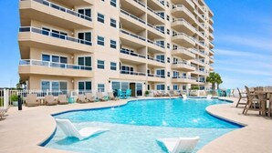 A multi-story hotel with a swimming pool, lounge chairs, and a palm tree. - Stunning 3BR Beachfront Condo - Heated Pool - Orange Beach Enclave #405 (Orange Beach)