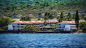 A coastal hotel with multiple buildings, a rocky shoreline, and lush greenery in the background. - 🏖️Partial Ocean View Kona Condo | Larger Lanai + AC (Kailua Kona)