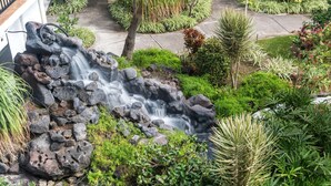 A waterfall feature surrounded by lush greenery and a paved pathway. - 🏖️Partial Ocean View Kona Condo | Larger Lanai + AC (Kailua Kona)