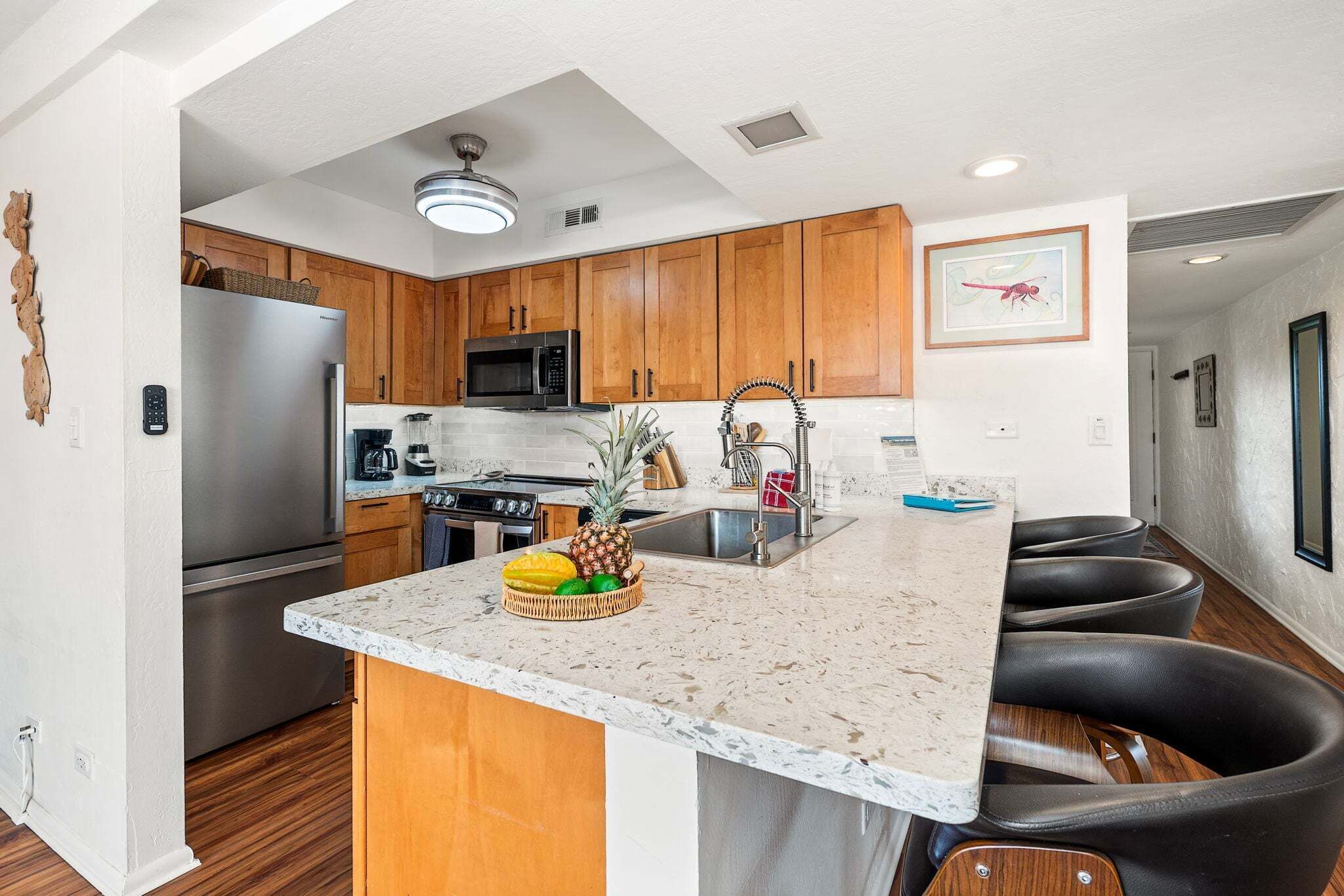 A modern kitchen with wooden cabinets, stainless steel appliances, a granite countertop, and a fruit bowl.