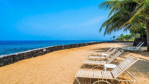 A beach with sun loungers, a palm tree, and a stone wall. - 🏖️Partial Ocean View Kona Condo | Larger Lanai + AC (Kailua Kona)