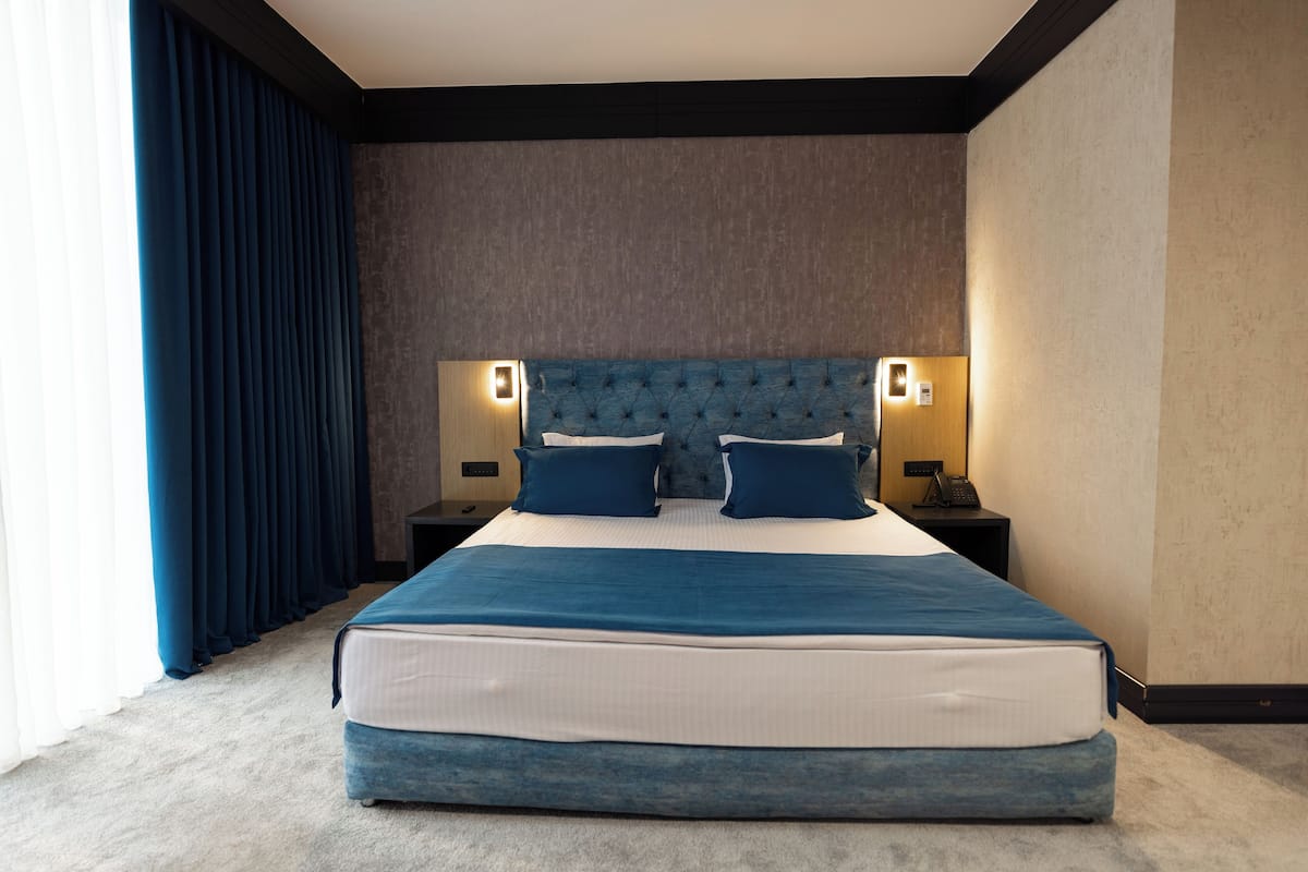 Una cama grande con cabecera capitonada, dos mesitas de noche con lámparas, y vista al interior de la habitación.