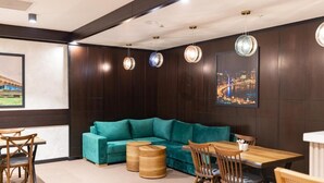 Eine moderne Lounge mit einem türkisblauen Sofa, Holzsesseln, einem Holztisch und einem Stadtbild an der Wand.