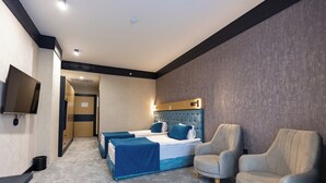 Ein Hotelzimmer mit einem Bett, zwei Sesseln, einem Fernseher und Teppichboden.