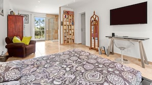 A spacious bedroom with a large bed, a TV mounted on the wall, a bookshelf, and a glass shower area. - Guest Room 'Chambre 2 Chine' with Shared Pool, Wi-Fi, and Air Conditioning (Cotignac)