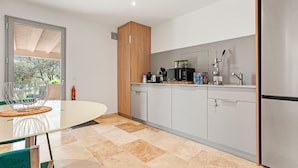 A modern kitchen with grey cabinets, a stainless steel refrigerator, and a dining area with a glass table and chairs. - Guest Room 'Chambre 2 Chine' with Shared Pool, Wi-Fi, and Air Conditioning (Cotignac)