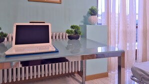 Ein modernes Zimmer mit Glastisch, Laptop, Heizkörper, Topfpflanze und einem gerahmten Bild an der Wand.