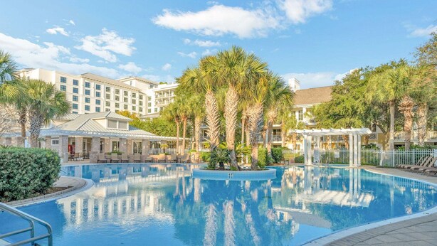 Piscina cercada por palmeiras e um prédio de hotel.