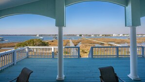 Una terraza techada con barandillas y columnas blancas, con vistas a la costa y una perspectiva clara del agua y edificios distantes.