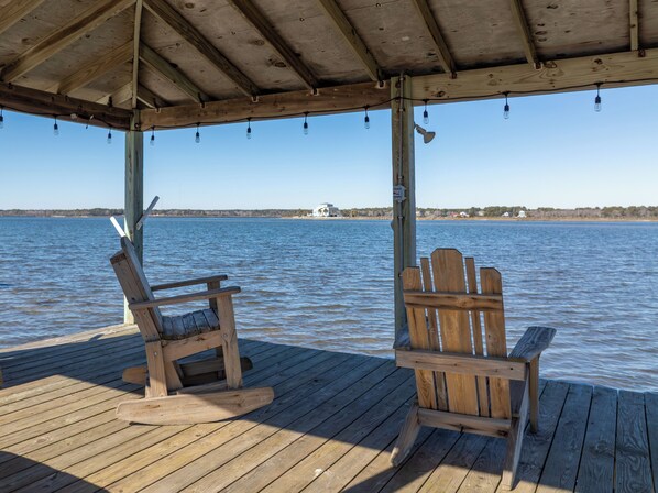 Een houten terras met twee Adirondack-stoelen gericht op een waterpartij.