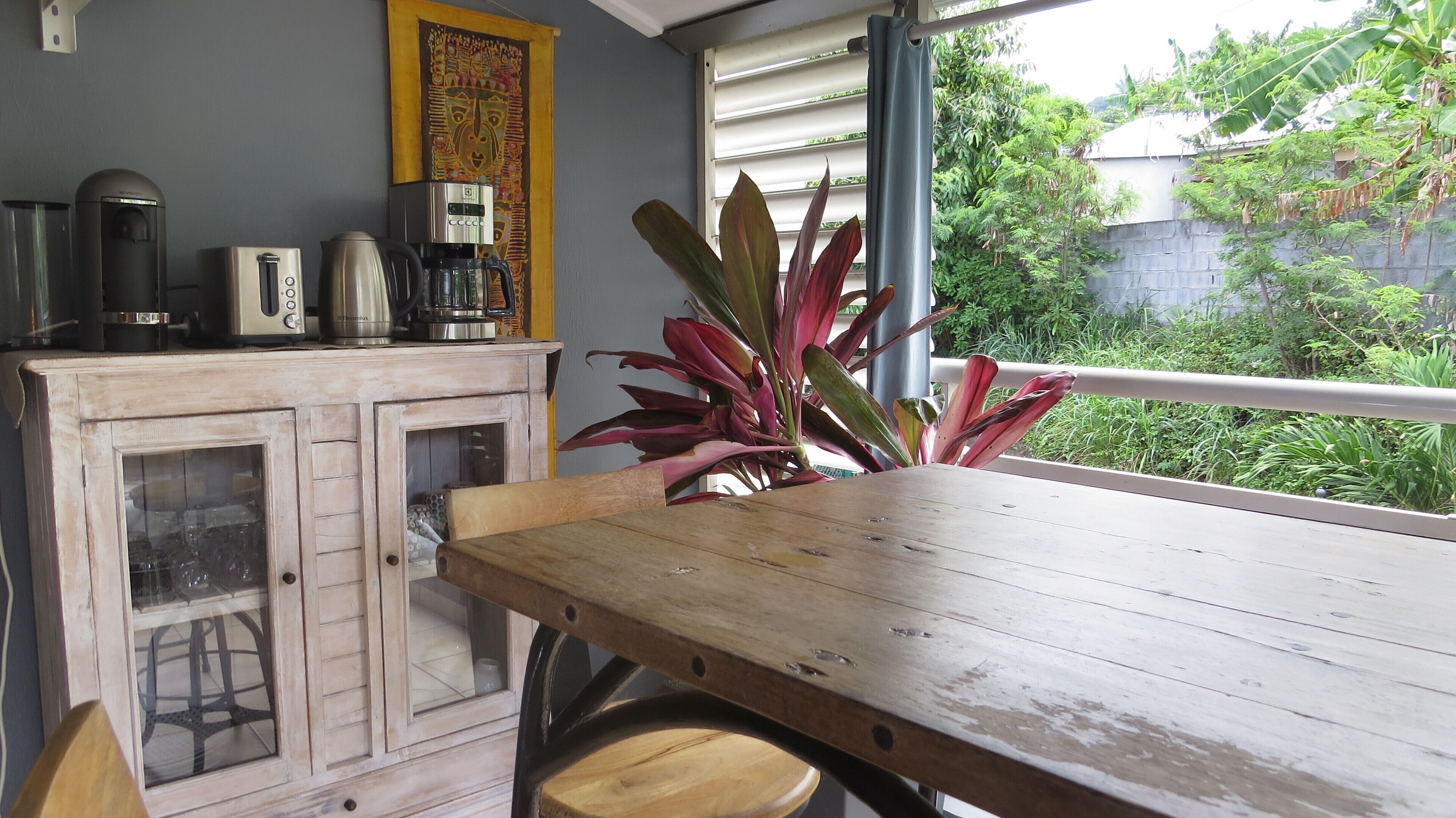 A wooden table with a potted plant, a cabinet with glass doors, and a coffee maker on a shelf.