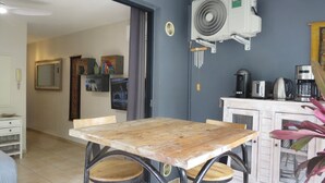 Ein Essbereich mit einem Holztisch und Stühlen, eine Küche mit Geräten und eine Wandklimaanlage.