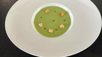 Une assiette blanche contenant une soupe verte et des croûtons, le tout posé sur une surface noire.
