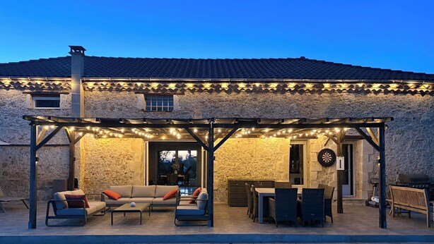 Un edificio de piedra con piscina, zona de estar exterior y guirnaldas de luces.