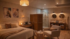 Un dormitorio moderno con una cama grande, un armario de madera, una zona de estar con una silla, una mesita redonda pequeña y un tocador con espejo y lavabo.