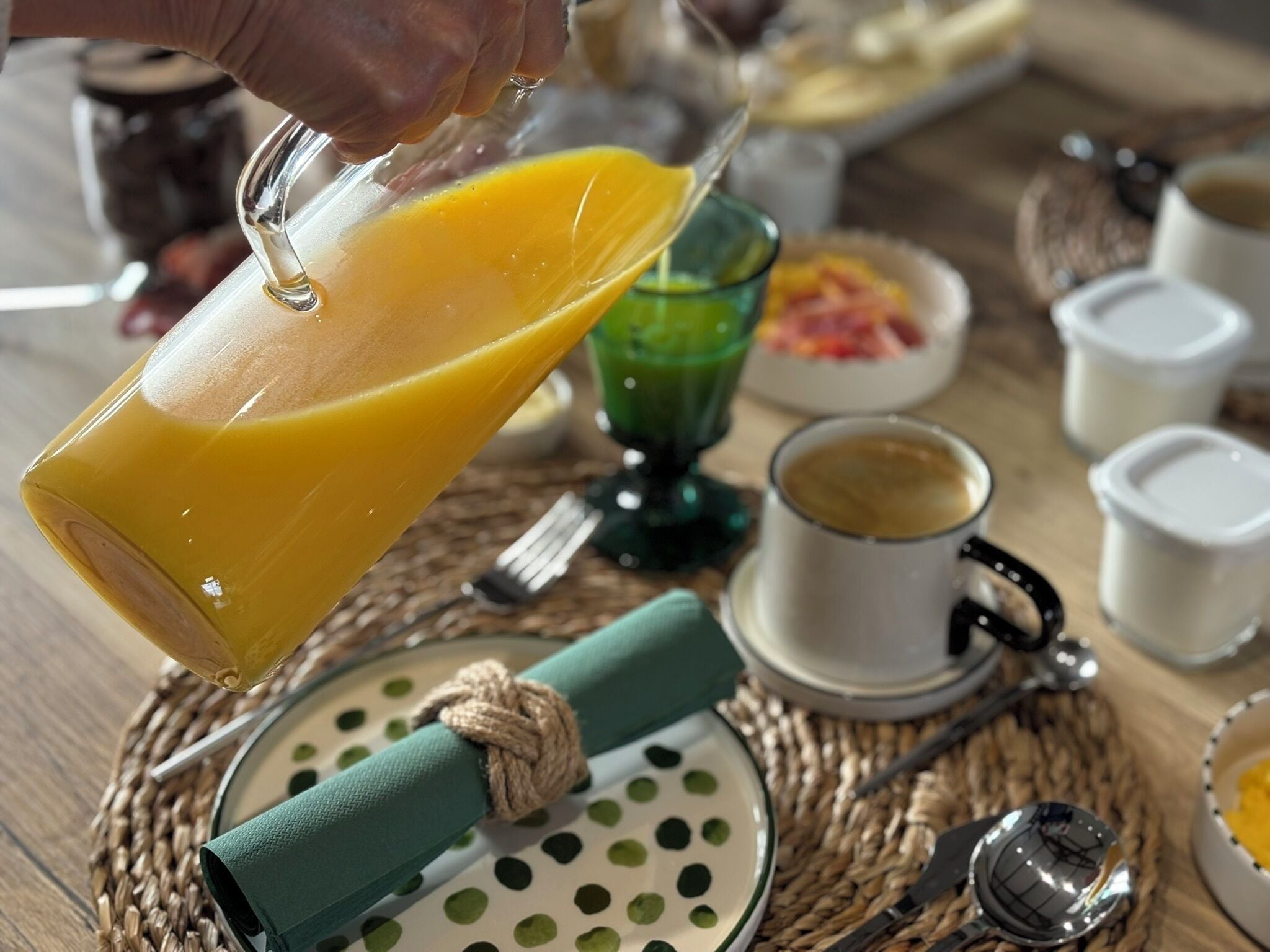 A breakfast setting with a glass of orange juice, a green polka dot plate, and a woven placemat.
