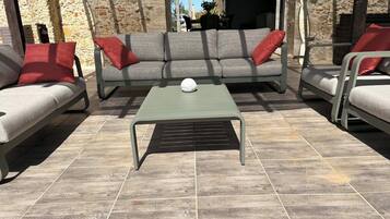 An outdoor seating area with a grey sofa, red cushions, and a green table with a white spherical object on it.