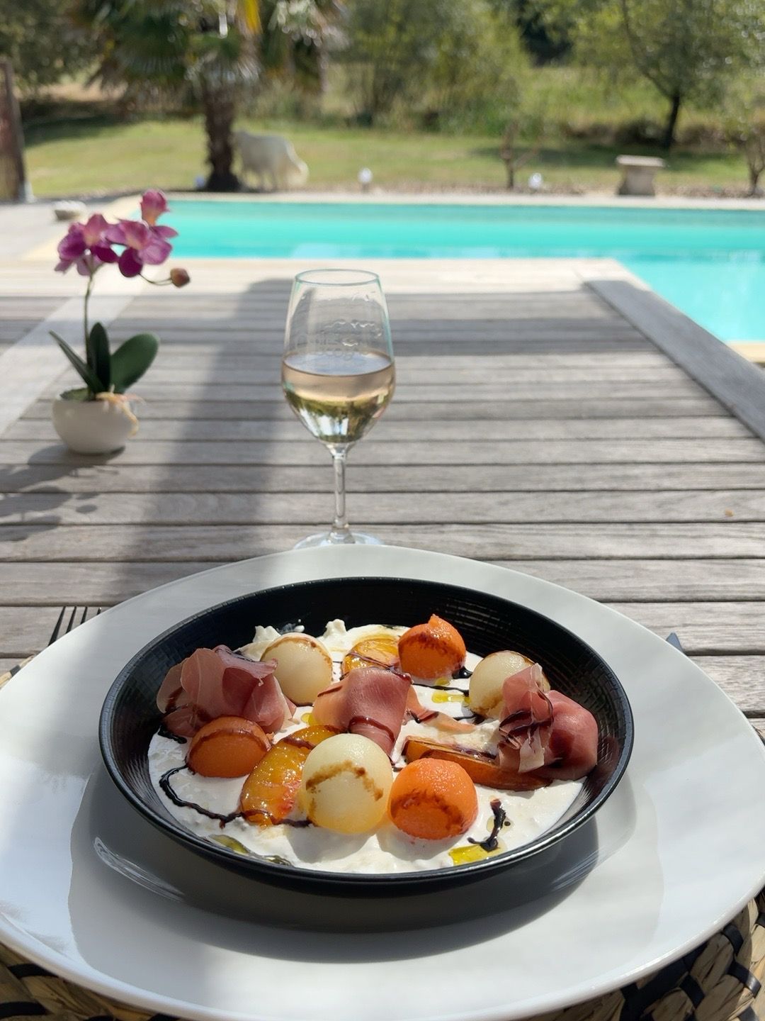 Une table à manger avec une assiette de nourriture et un verre de vin blanc.