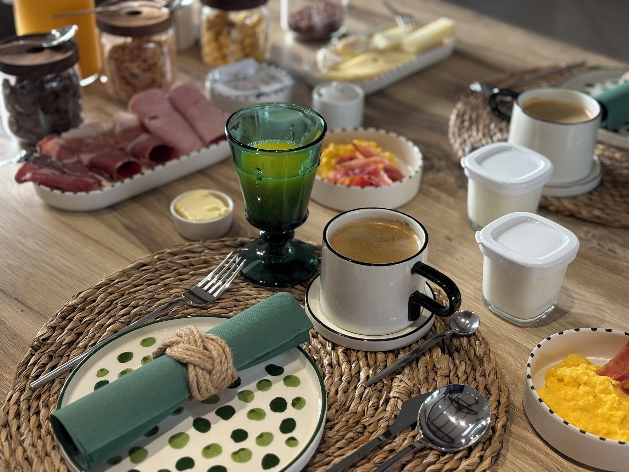 A breakfast setting with plates of food, a glass of green juice, and coffee cups.