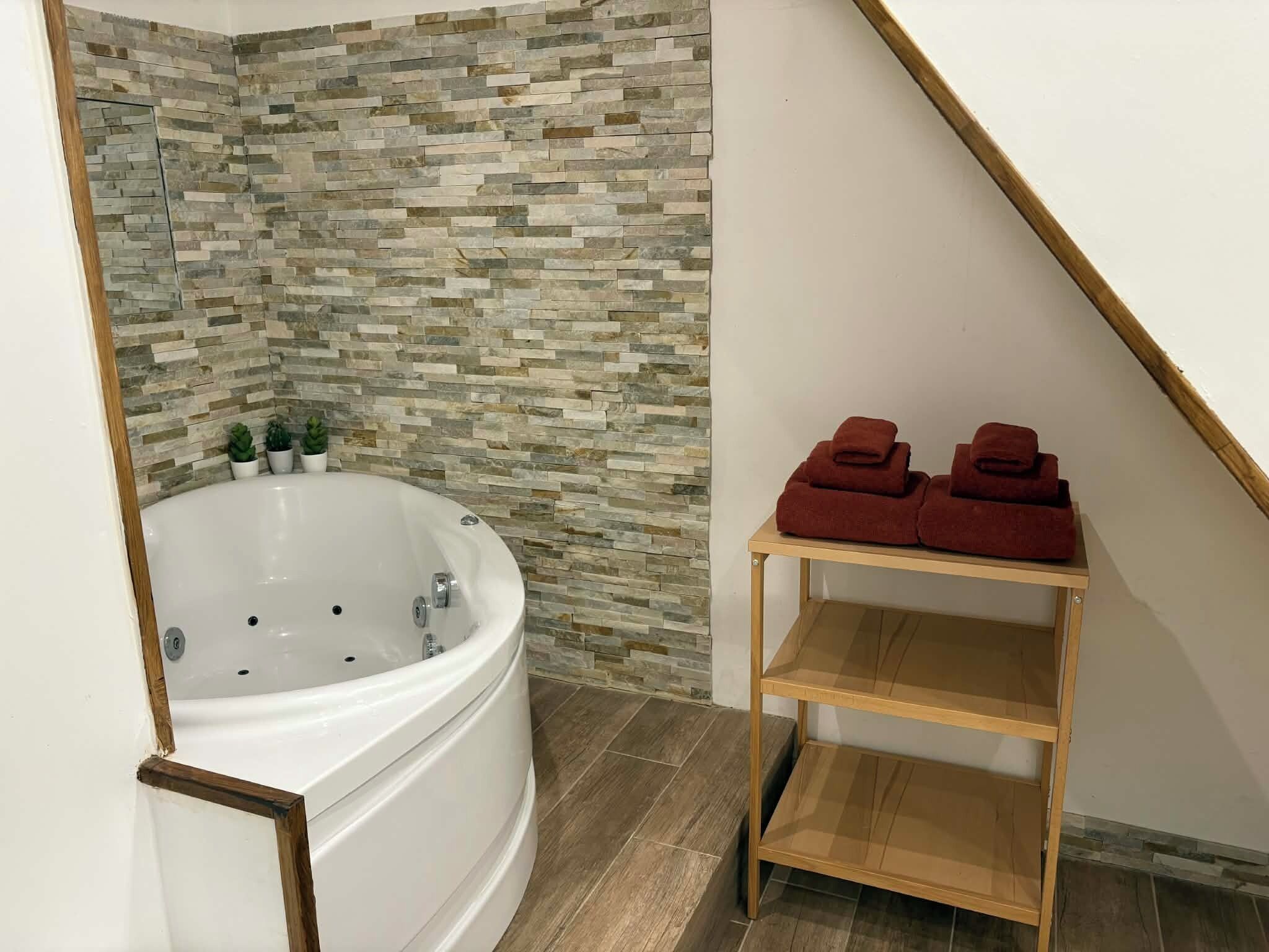 Un baño moderno con una bañera independiente, un muro de mosaico de piedra y un estante de madera con toallas.