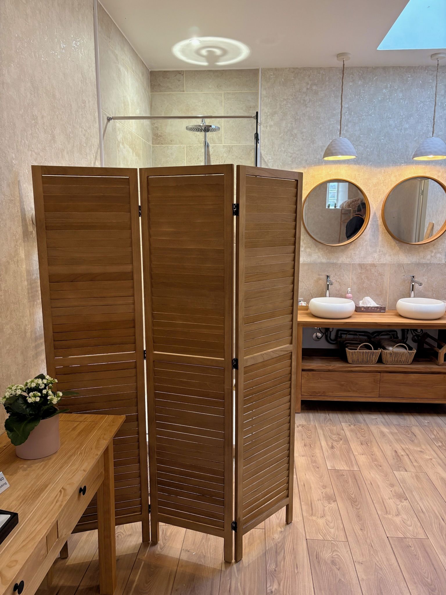 Un baño con separador de madera, dos lavamanos, un espejo y una lámpara en el techo.