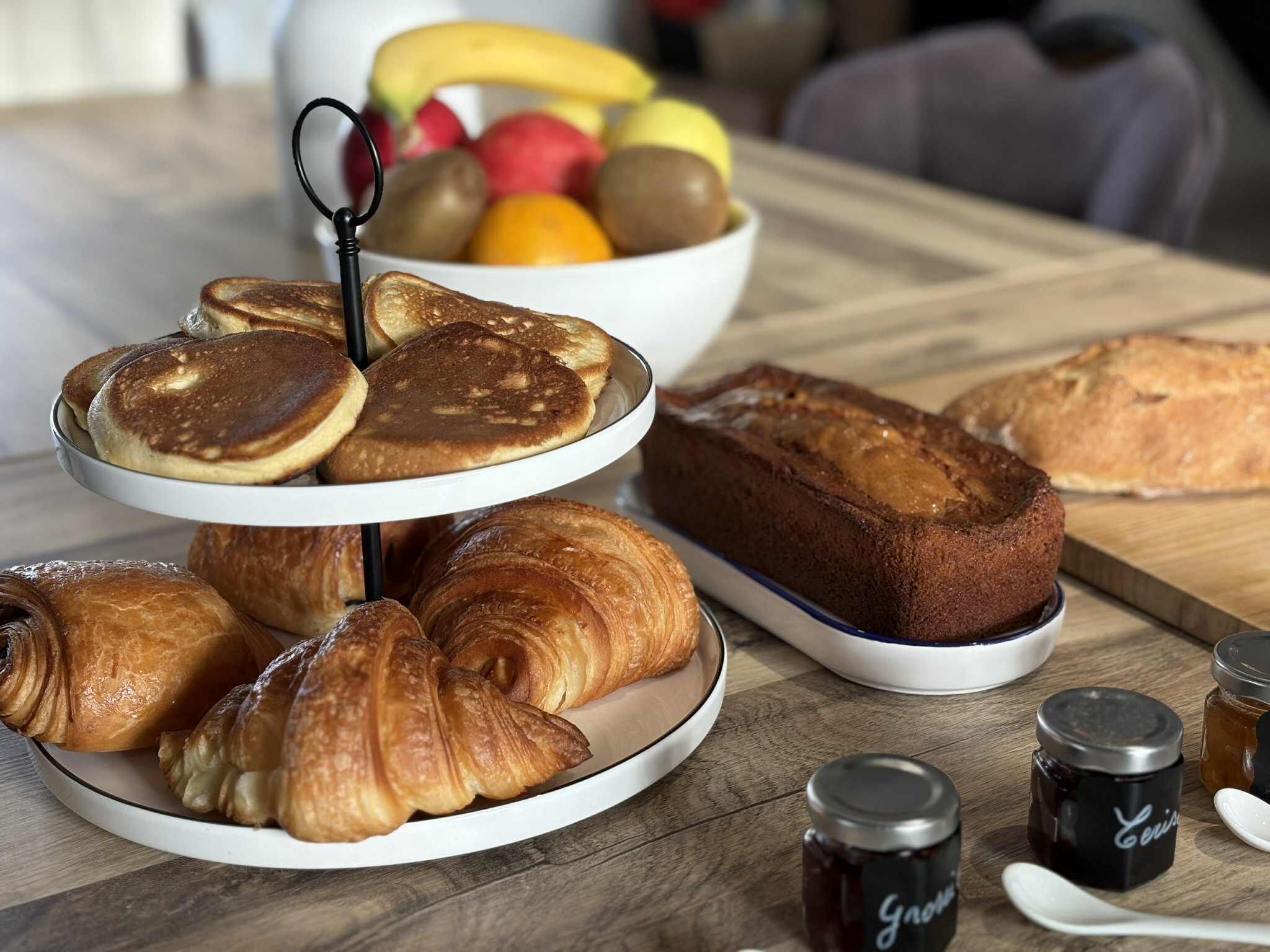 Desayuno con tortitas, croissants y una hogaza de pan sobre una mesa de madera.