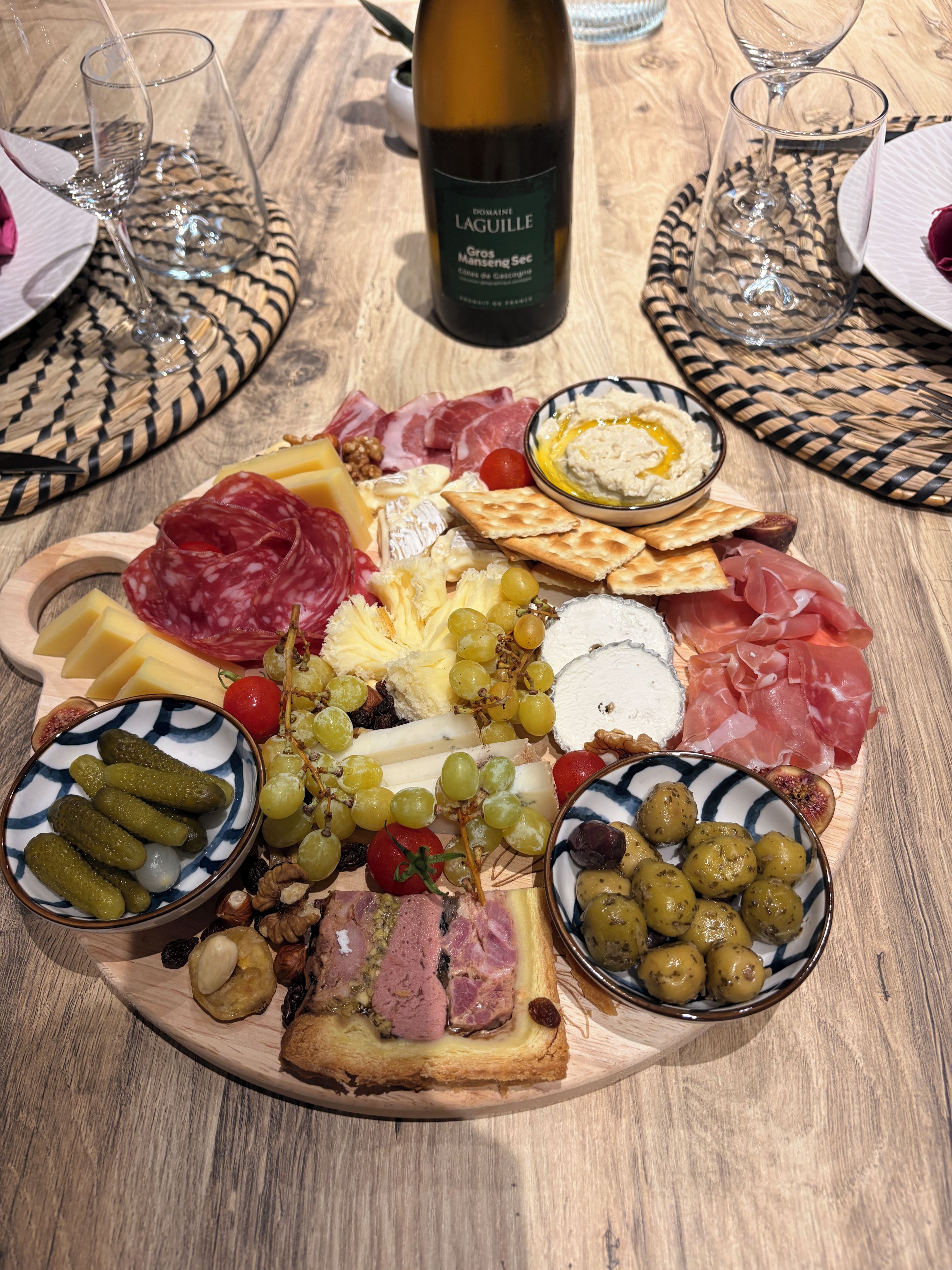 Un tagliere con formaggi, salumi e frutta di vario tipo su un tavolo di legno.