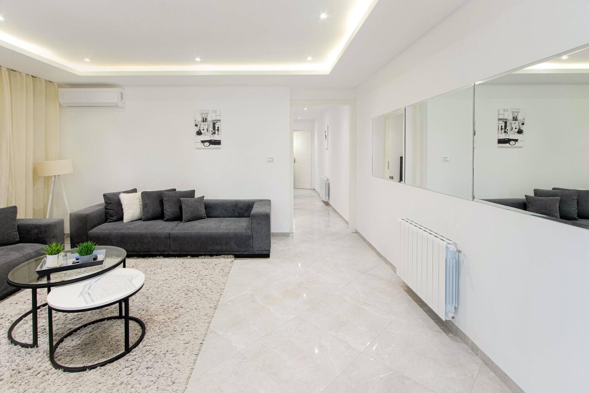 A modern living room with a grey sofa, a round coffee table, and a large mirror.