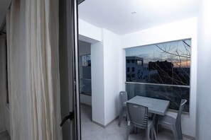 Un balcone con tavolo e sedie, vista su edifici e una porta con tenda.