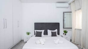 Een moderne slaapkamer met een groot bed, witte muren, een donkere hoofdbord en een raam met gordijnen.