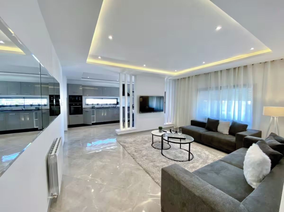 A modern living room with a grey sofa, a coffee table, and a TV mounted on the wall.