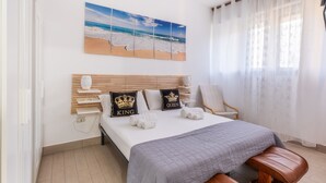 A bedroom with a bed, a headboard, a bedside table, a chair, a window with sheer curtains, and a beach-themed artwork on the wall. - Rossini 14 | Downtown and Beach Within Walking Distance (Porto Cesareo)