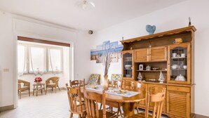 A dining area with a wooden table and chairs, a cabinet with glass doors, and a window with curtains. - Rossini 14 | Downtown and Beach Within Walking Distance (Porto Cesareo)
