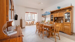 A spacious dining area with wooden furniture, a kitchen with wooden cabinets, and a view through a window. - Rossini 14 | Downtown and Beach Within Walking Distance (Porto Cesareo)