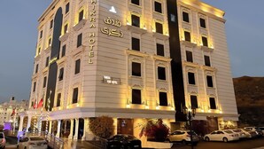 Un hôtel à plusieurs étages, doté d’une enseigne lumineuse, d’une entrée imposante et d’un parking où sont stationnées plusieurs voitures.