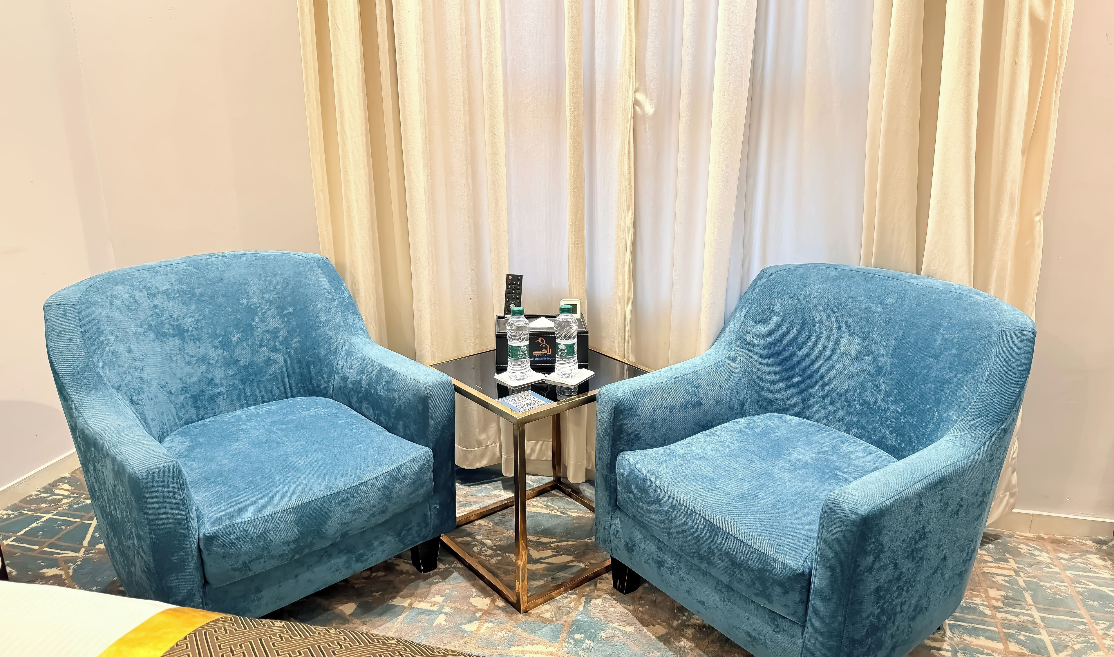 Two blue armchairs facing each other with a small table between them, holding a remote control, two water bottles, and a QR code.