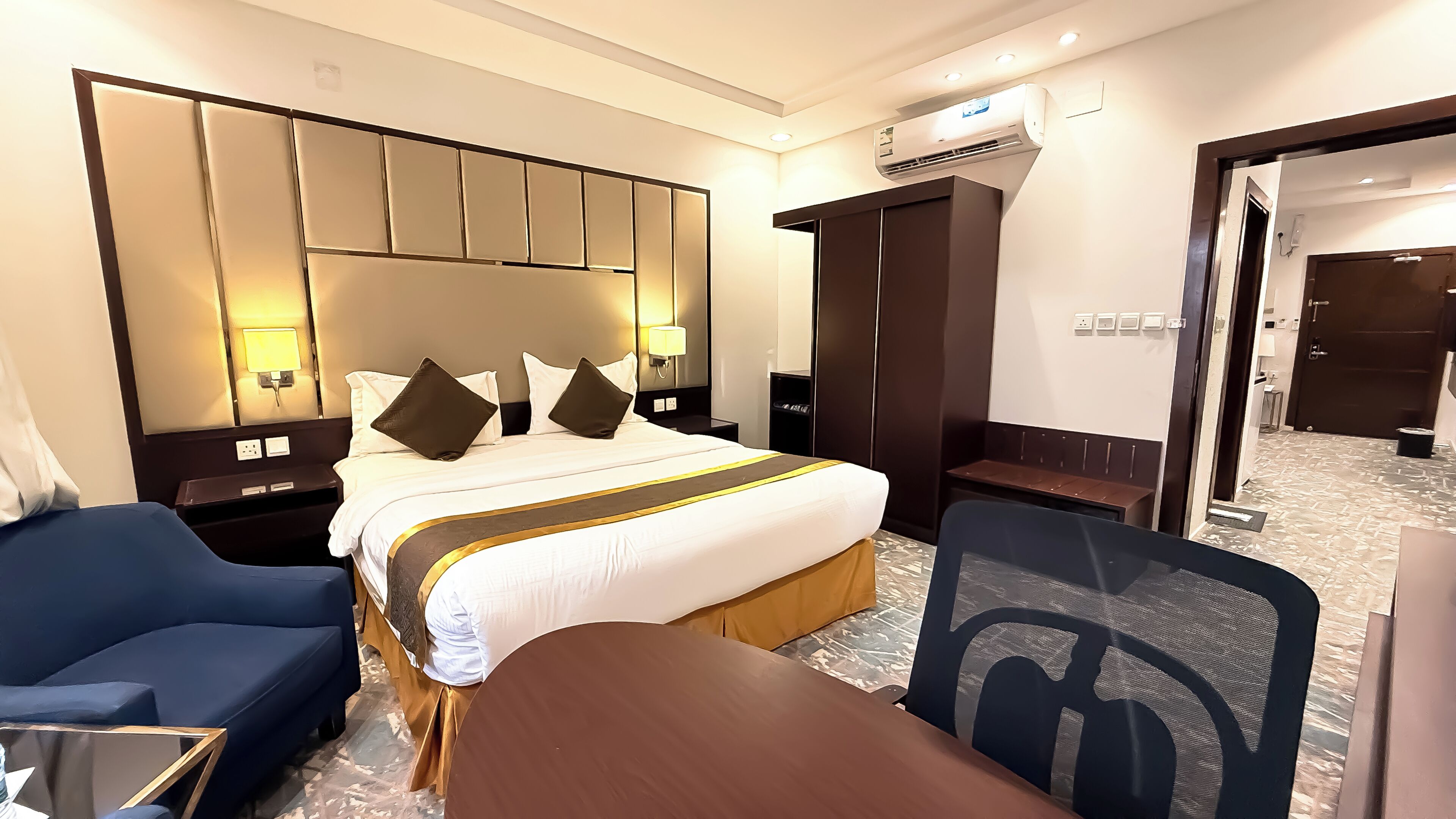 A hotel room with a large bed, a desk, a chair, and a wardrobe.