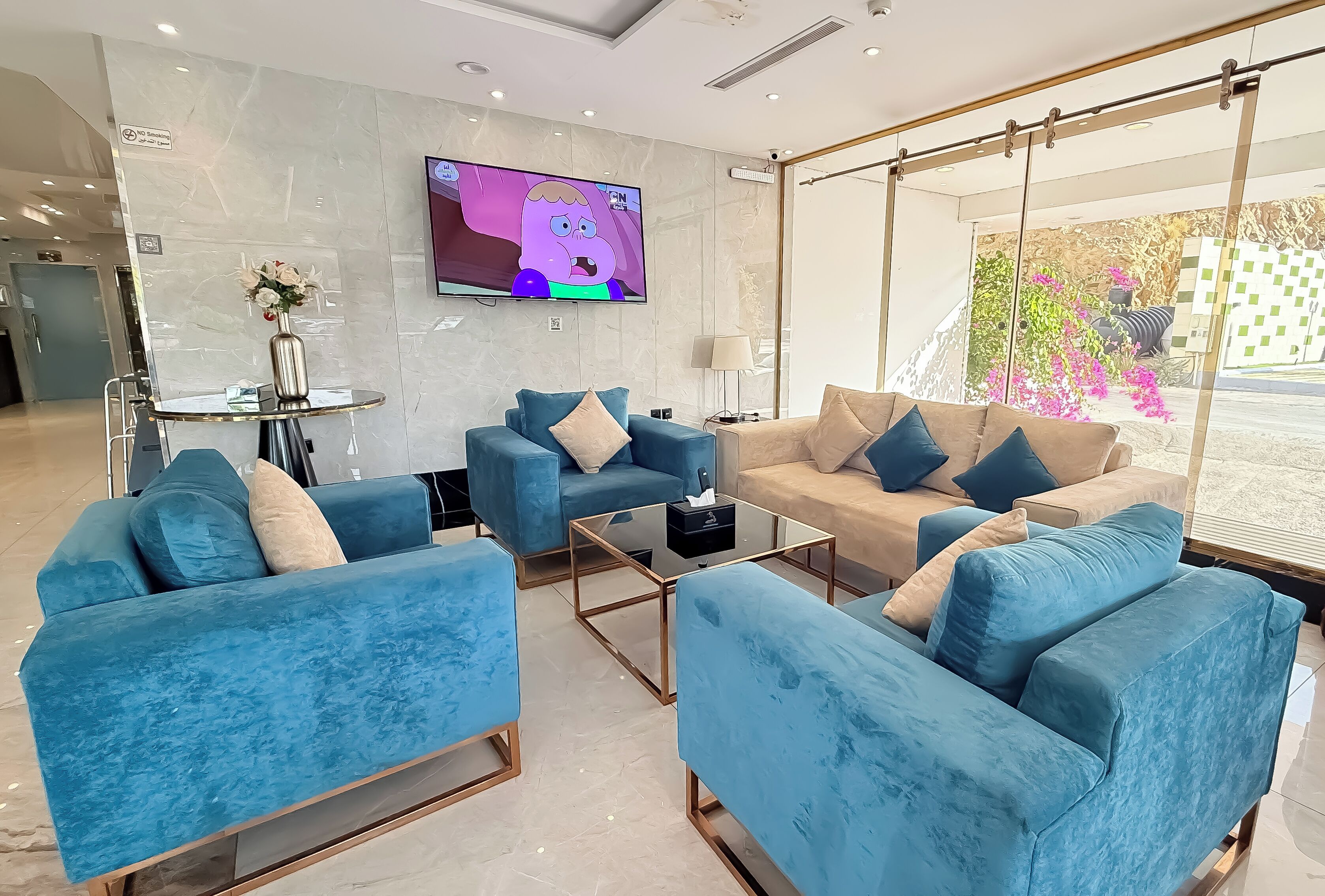 A modern hotel lobby with blue sofas, a TV, and a large window with a view of greenery.