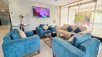 A modern hotel lobby with blue sofas, a TV, and a large window with a view of greenery.