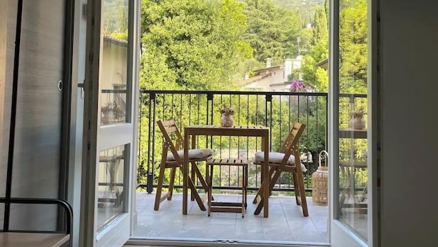 An open balcony with a table and chairs, offering a view of a green landscape. - Suite Disposition - 555 Al Vittoriale (Gardone Riviera)