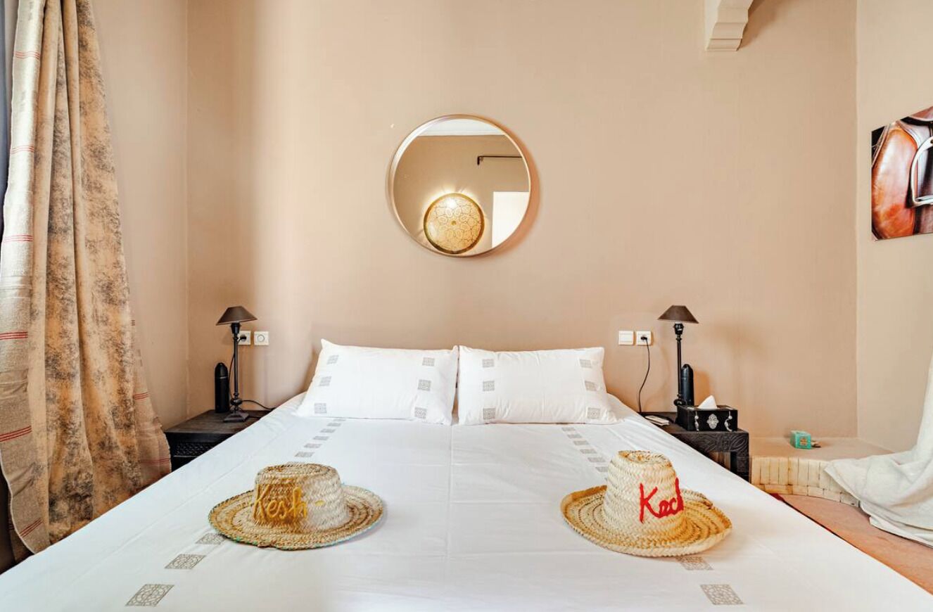 A hotel room with a large bed, two bedside lamps, a round mirror on the wall, and a framed picture on the wall.